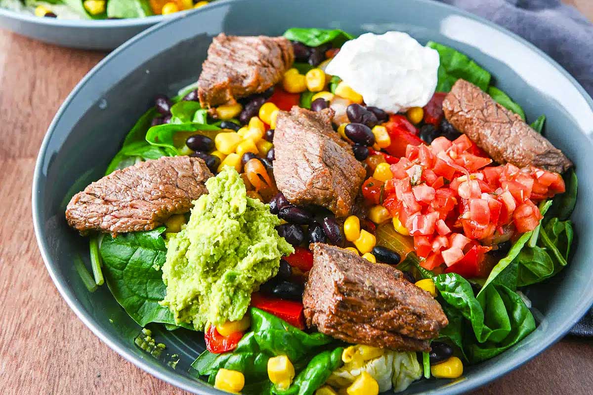 A bowl of steak salad with black beans, corn and sour cream.