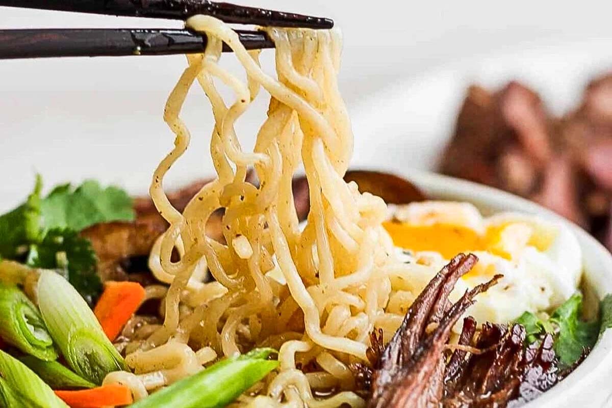 A slow cooker Asian noodle soup with chopsticks.