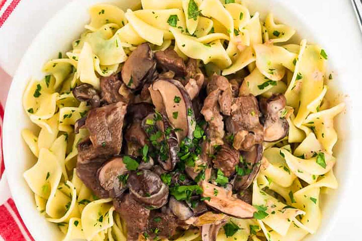 Beef stroganoff in a white bowl with mushrooms and parsley.