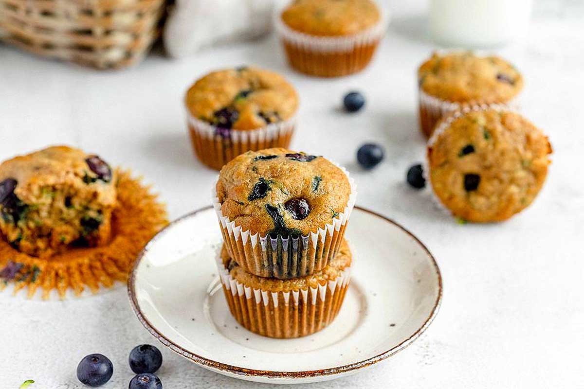 Blueberry muffins on a plate with a cup of zucchini-infused milk.