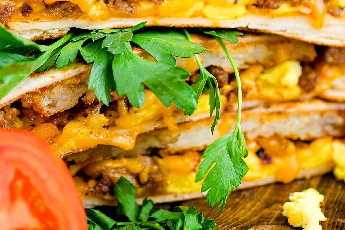 A stack of breakfast quesadillas on a wooden cutting board.