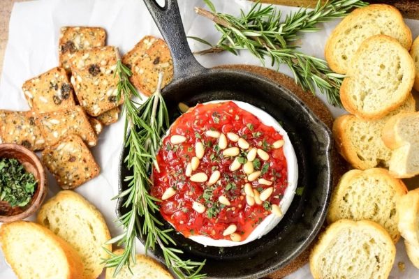 A skillet with a red sauce, bread and rosemary, perfect for brie recipes.