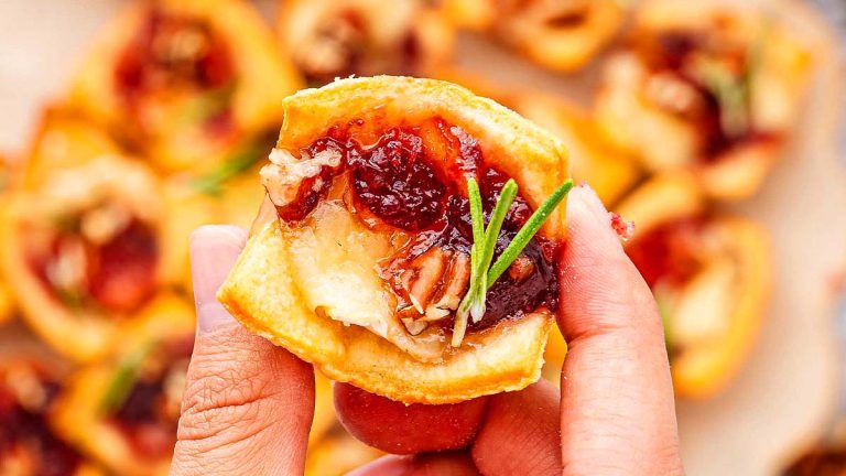 A person holding up a small fall appetizer with cranberry sauce.
