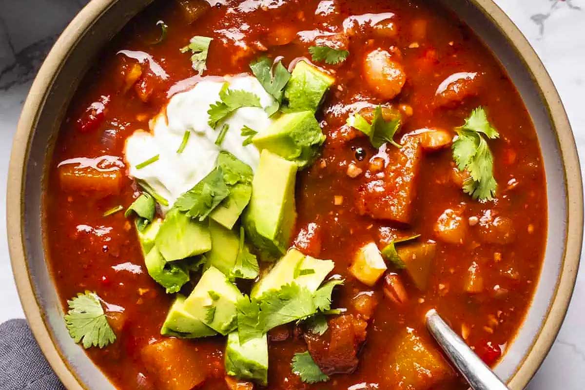 A comforting slow cooker soup, featuring a bowl of chili with creamy avocado and tangy sour cream.