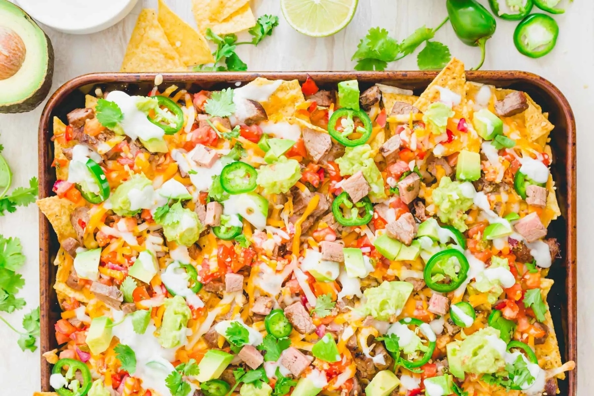 Nachos in a baking pan with shredded meat and avocado.