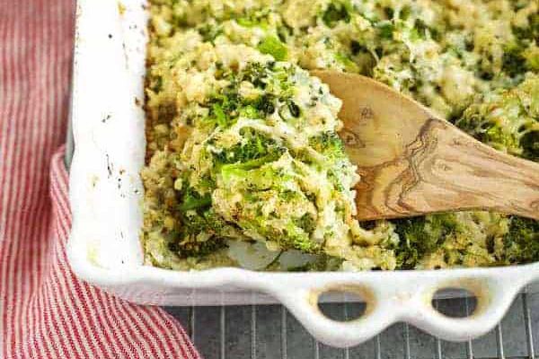 Broccoli casserole in a white dish with a wooden spoon.