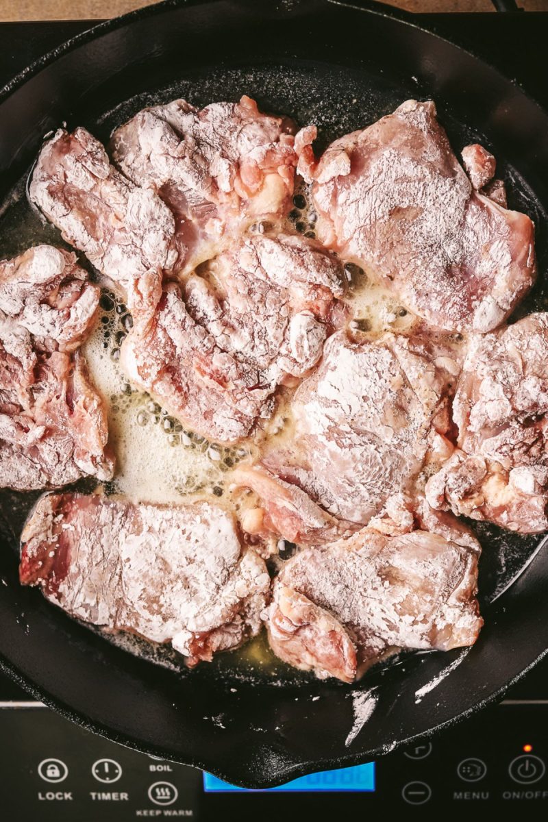 Pan-fried pork chops in a skillet on a stovetop.