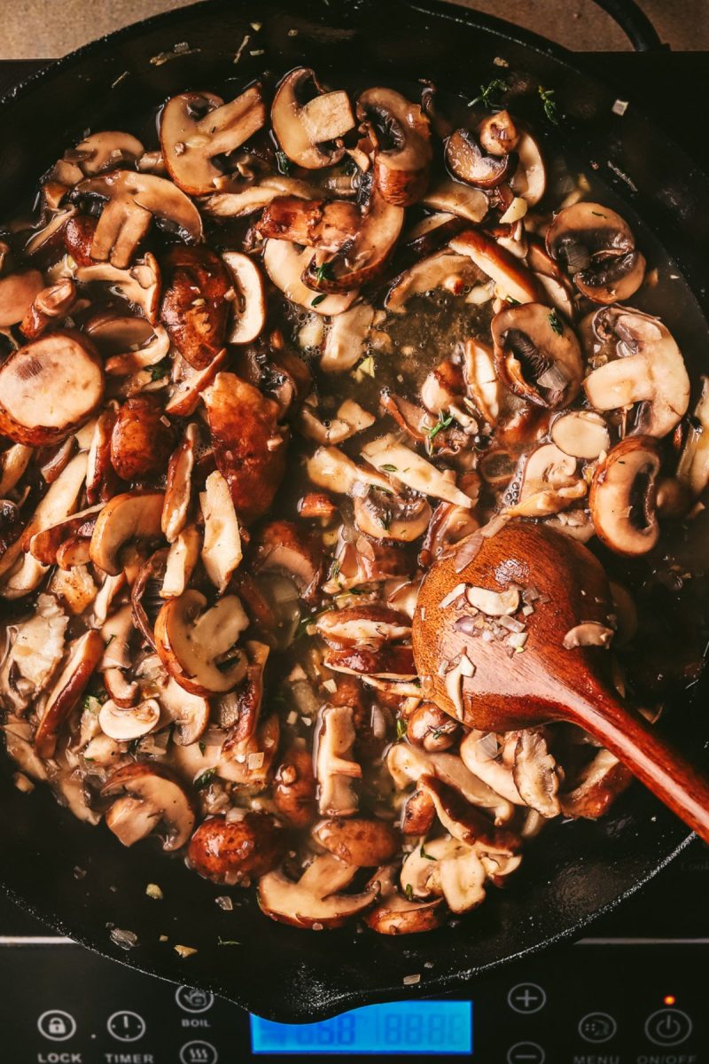 A skillet filled with mushrooms, champagne chicken, and a wooden spoon.