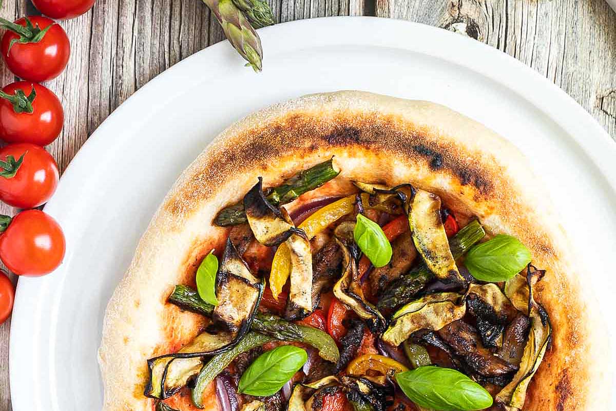 A pizza with vegetables and tomatoes on a plate.