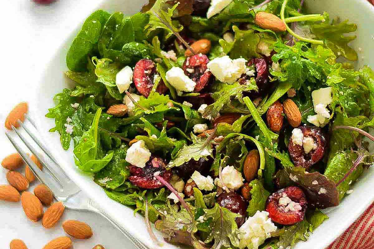 A salad with cranberries and almonds in a white bowl.