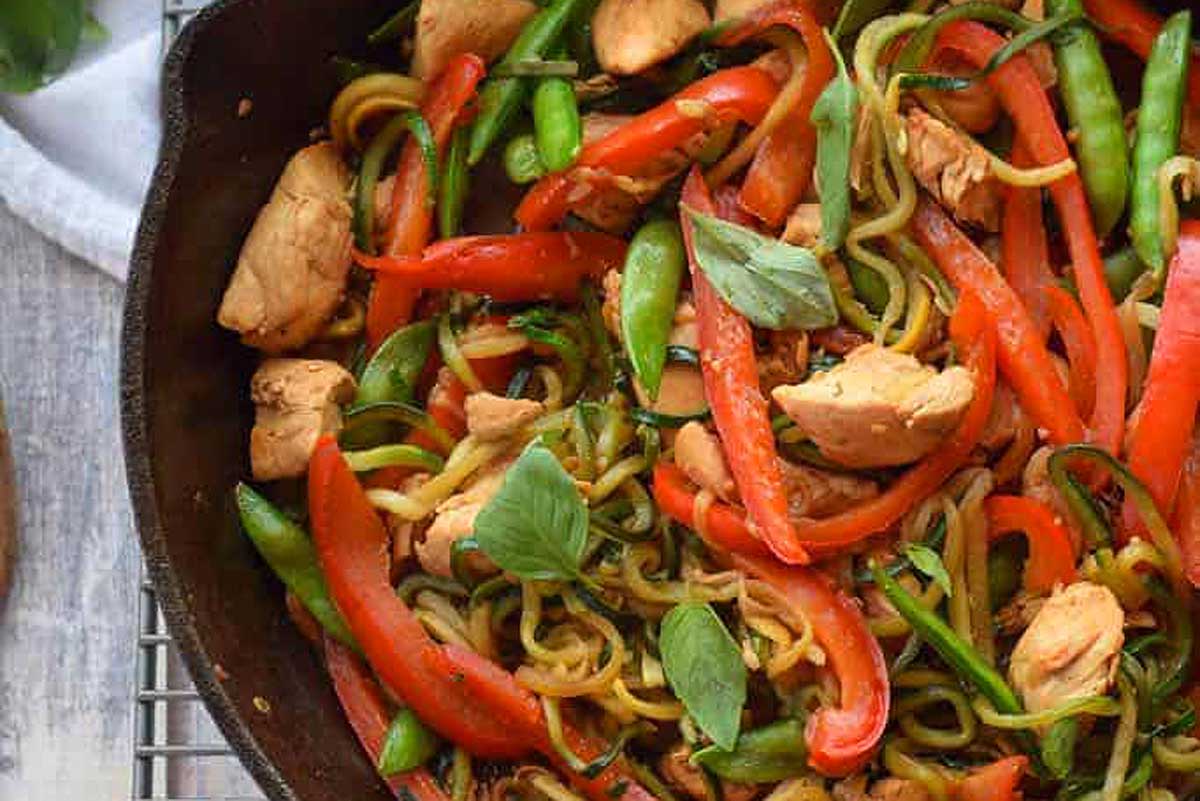 Stir fried noodles with chicken, zucchini, and vegetables in a skillet.