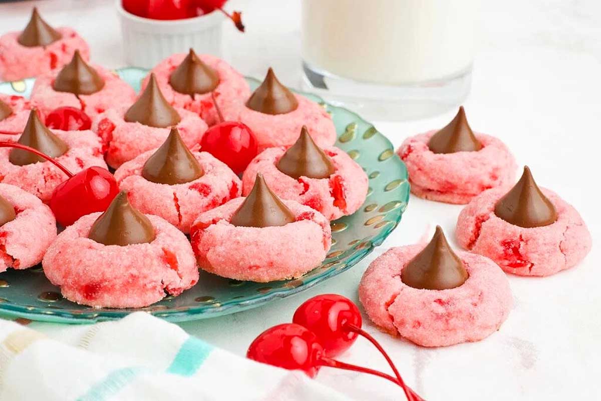 Pink cherry cookies on a plate with a glass of milk.
