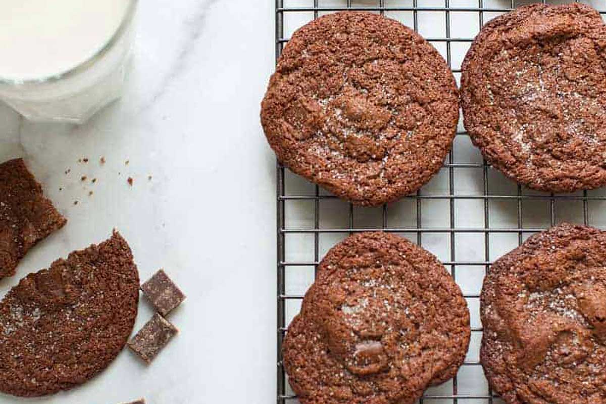 Chocolate cookies on a cooling rack with a glass of milk.