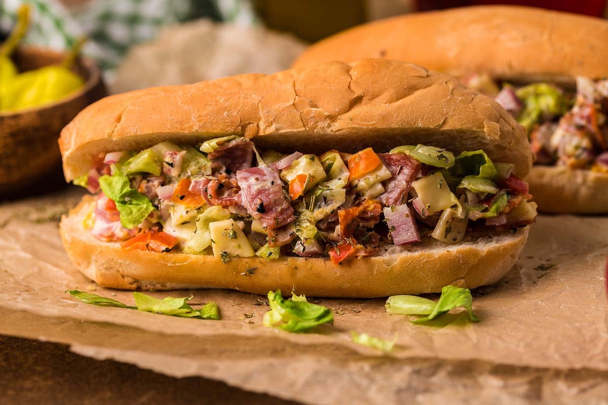 A sandwich served on a bun with meat, lettuce, tomatoes, and pickles.