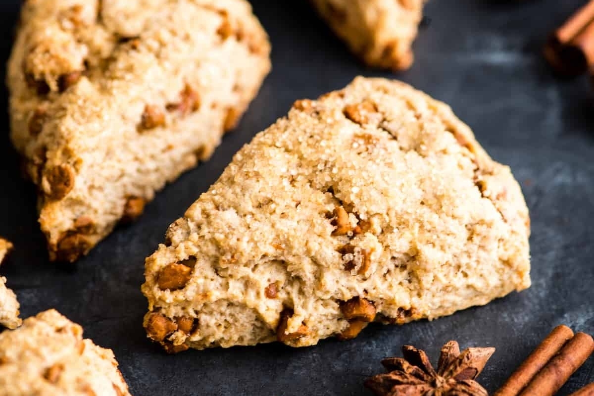 Cinnamon scones with cinnamon sticks on a black surface, perfect for holiday recipes.