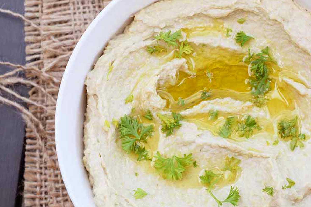 Hummus in a white bowl with parsley.