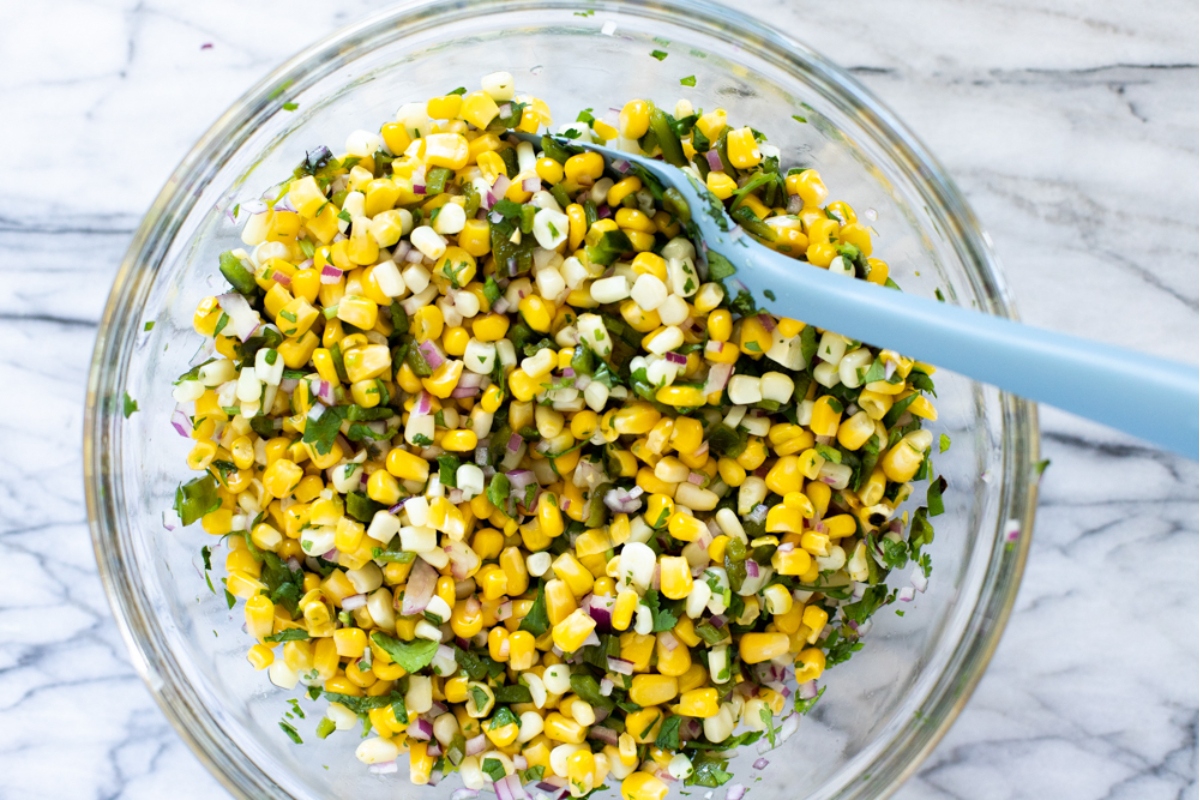 Corn salad in a glass bowl with a blue spoon.