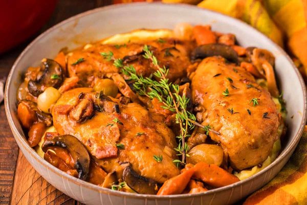 Roasted chicken with mushrooms and carrots in a white bowl.