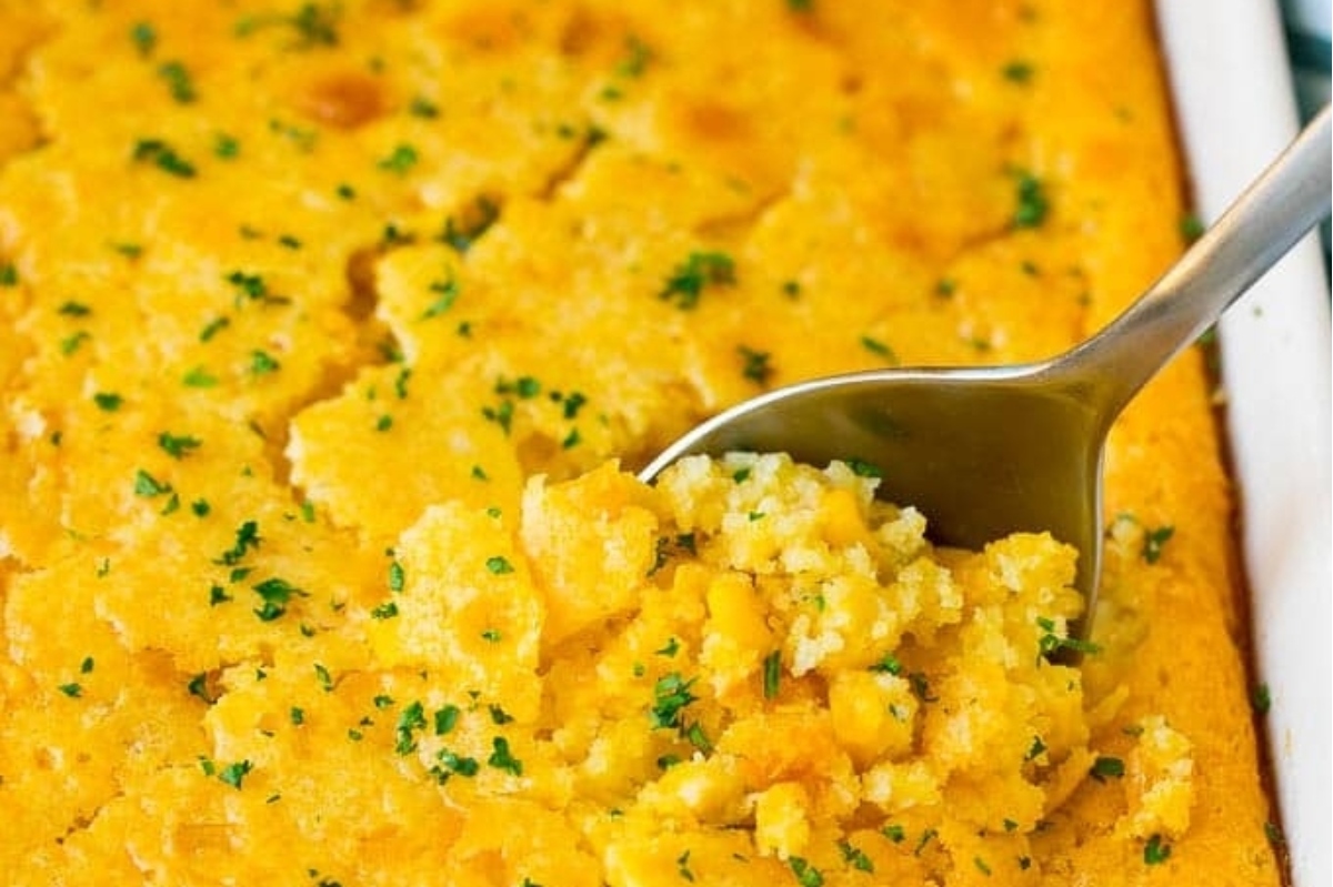 Cornbread casserole in a white dish with a spoon, served as a side dish.