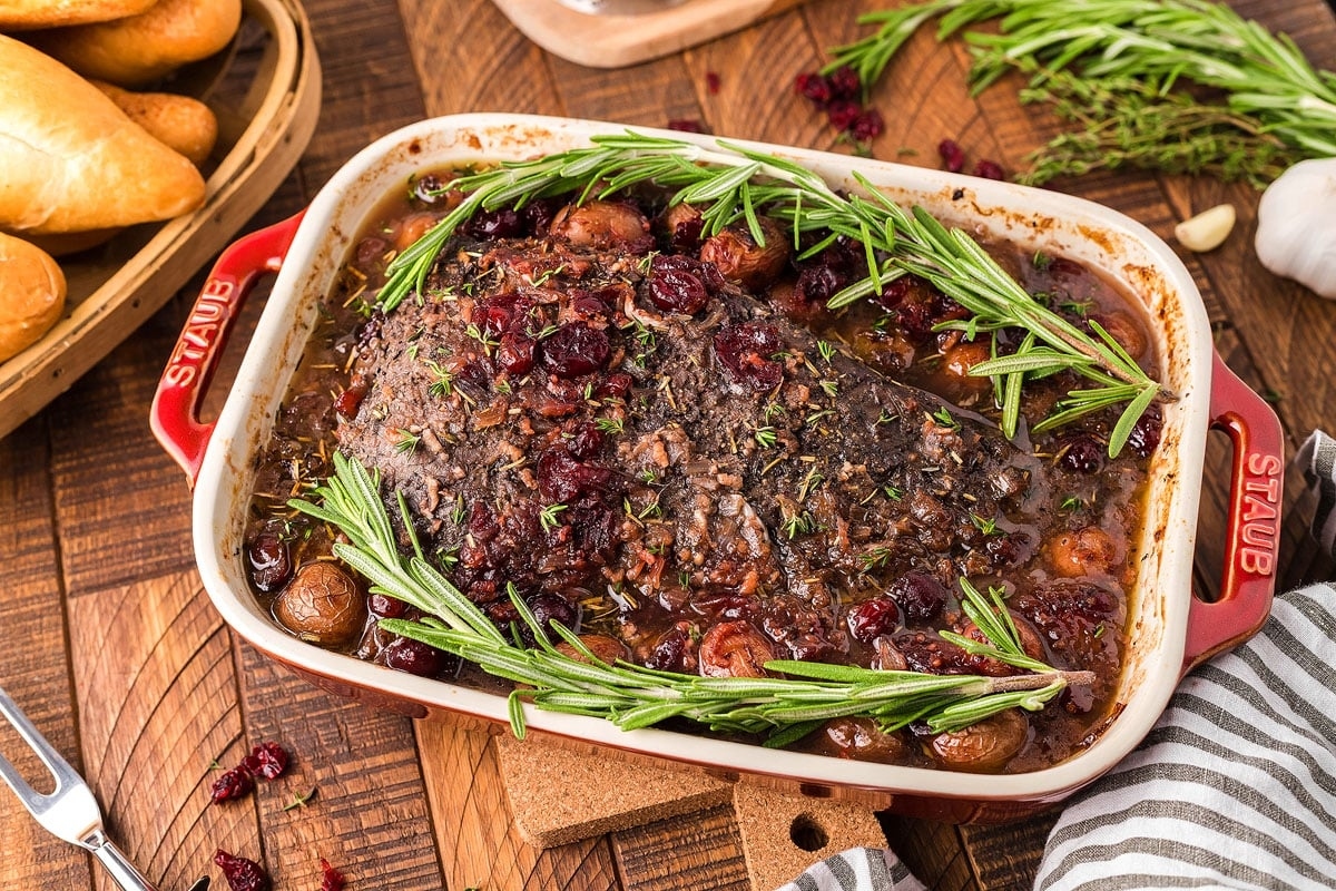 A beef brisket with rosemary and cranberries on a wooden table.