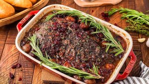 A Thanksgiving main dish roast with cranberries and rosemary on a wooden table.