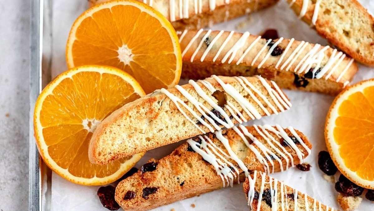Orange and raisin biscotti with a drizzle of white chocolate on a baking sheet.