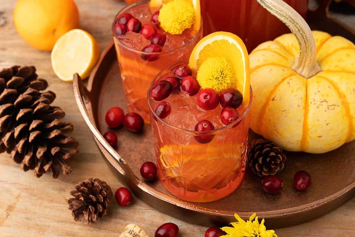 A tray of vegan Thanksgiving drinks with oranges, cranberries, and pine cones.