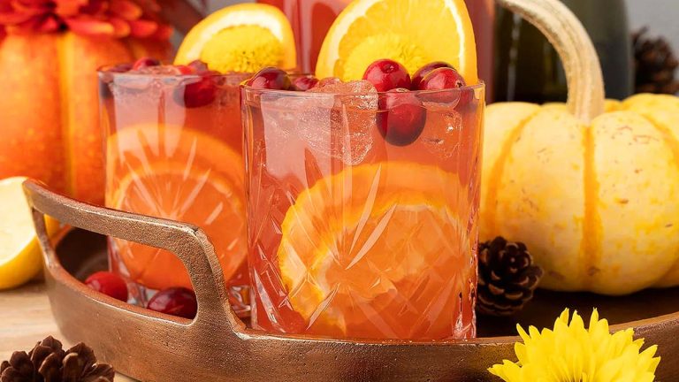 Two glasses of cranberry sangria on a tray with oranges and pumpkins, perfect for Thanksgiving cocktail recipes.
