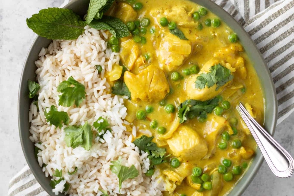A bowl of chicken curry with rice and Frozen peas.