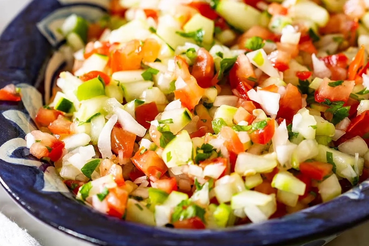 A bowl of mexican salsa with tomatoes and cucumbers.