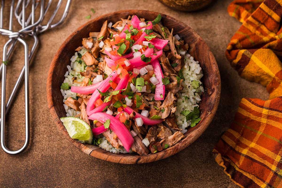 A bowl of rice with pork and radishes on it.