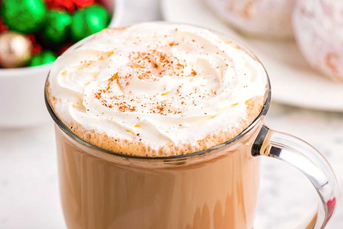 A cup of eggnog latte with whipped cream and sprinkles.