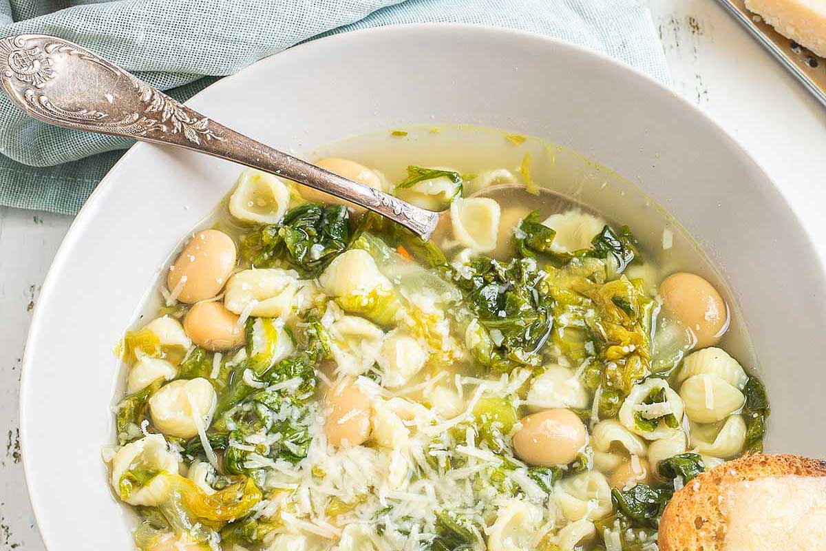 A bowl of pasta soup with broccoli and spinach.