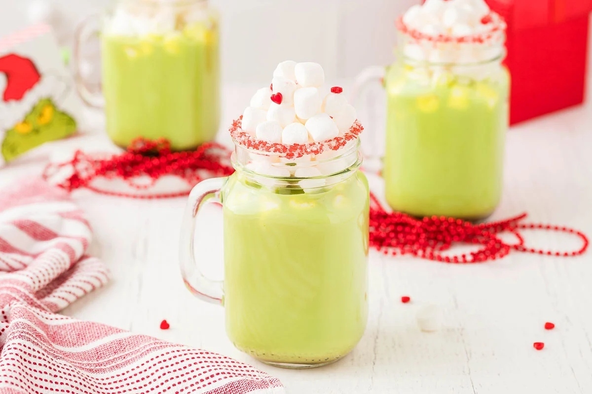 Three green mugs with whipped cream and Grinch recipes.