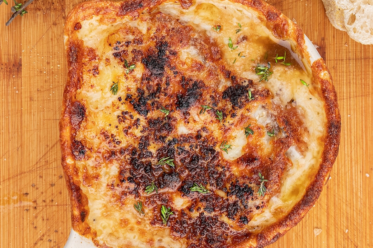 A warm and comforting dinner dish featuring melted cheese and freshly baked bread on a rustic wooden cutting board.