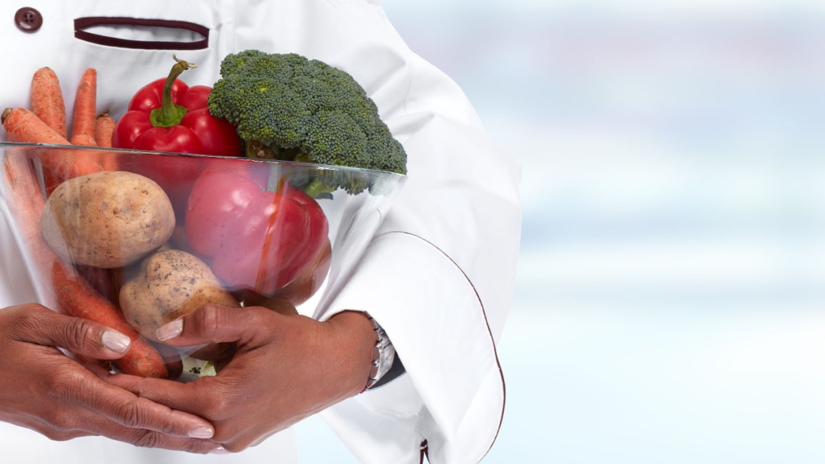 A chef in a white coat holding a bowl of vegetables.