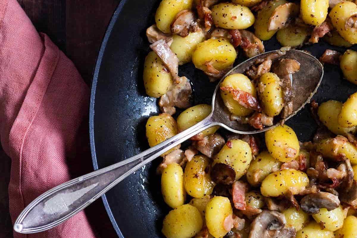 Potatoes and bacon in a skillet with a spoon.