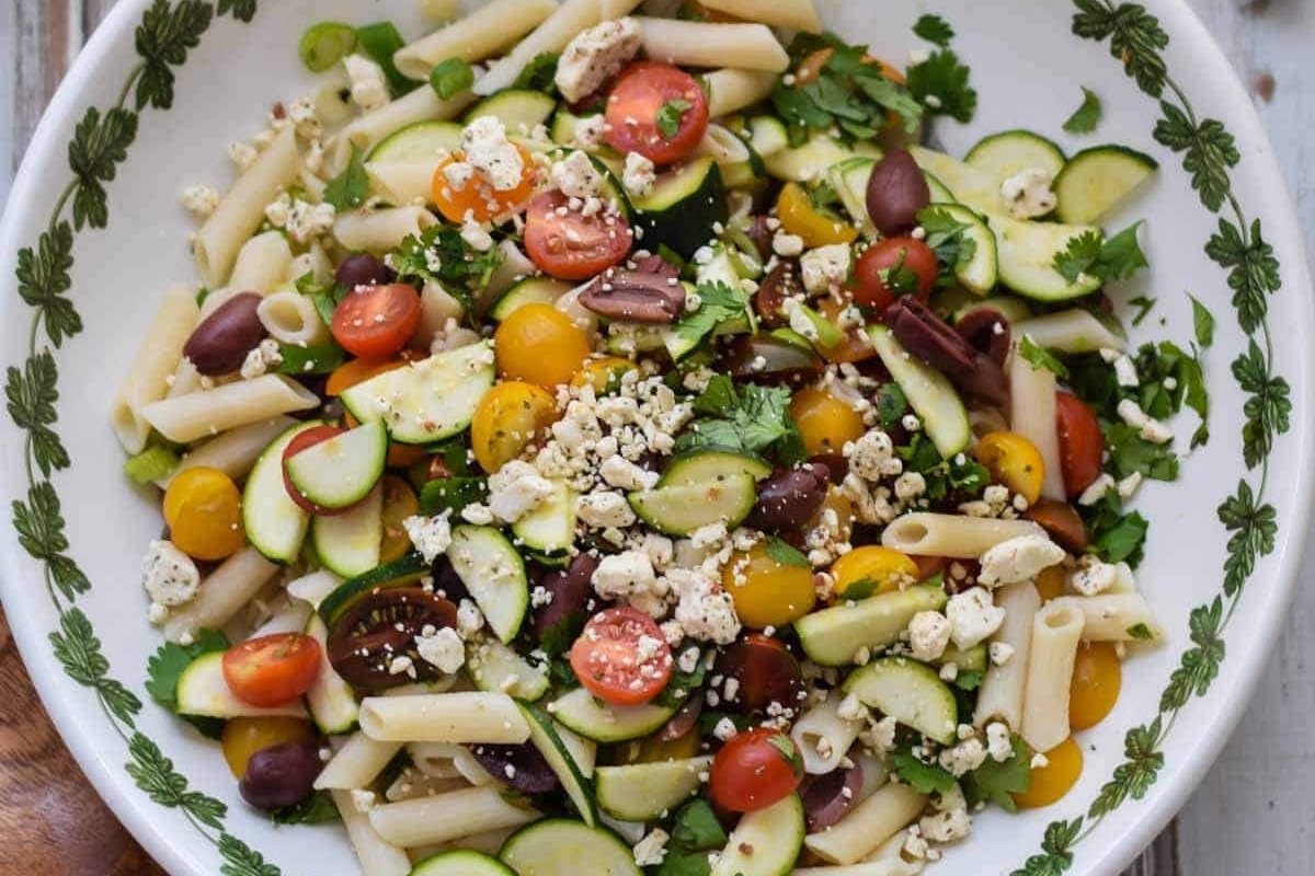 A bowl of pasta salad with tomatoes, cucumbers and feta cheese.