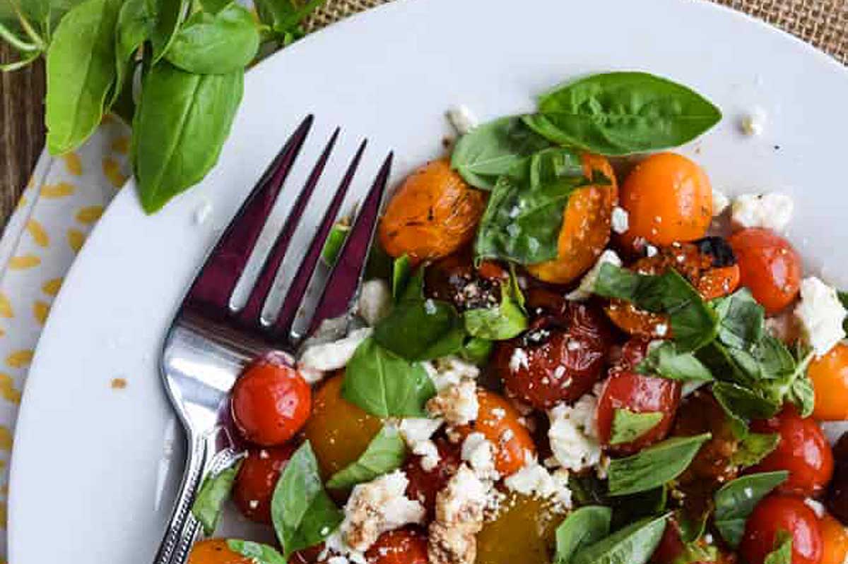 Grilled tomatoes with feta and basil on a white plate. This simple and delicious tomato recipe combines the smoky flavors of grilled tomatoes with the creamy saltiness of feta cheese and the fresh,