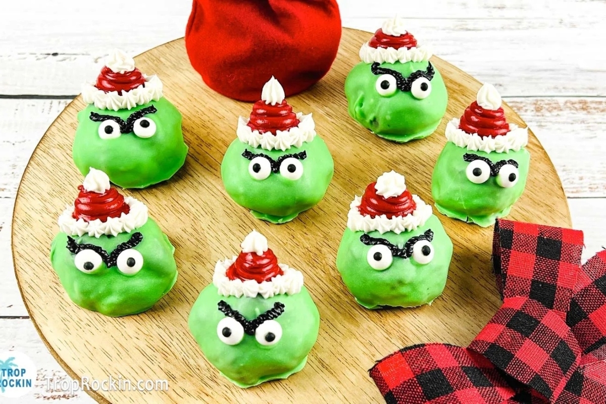 Christmas Grinch cake pops displayed on a wooden plate.
