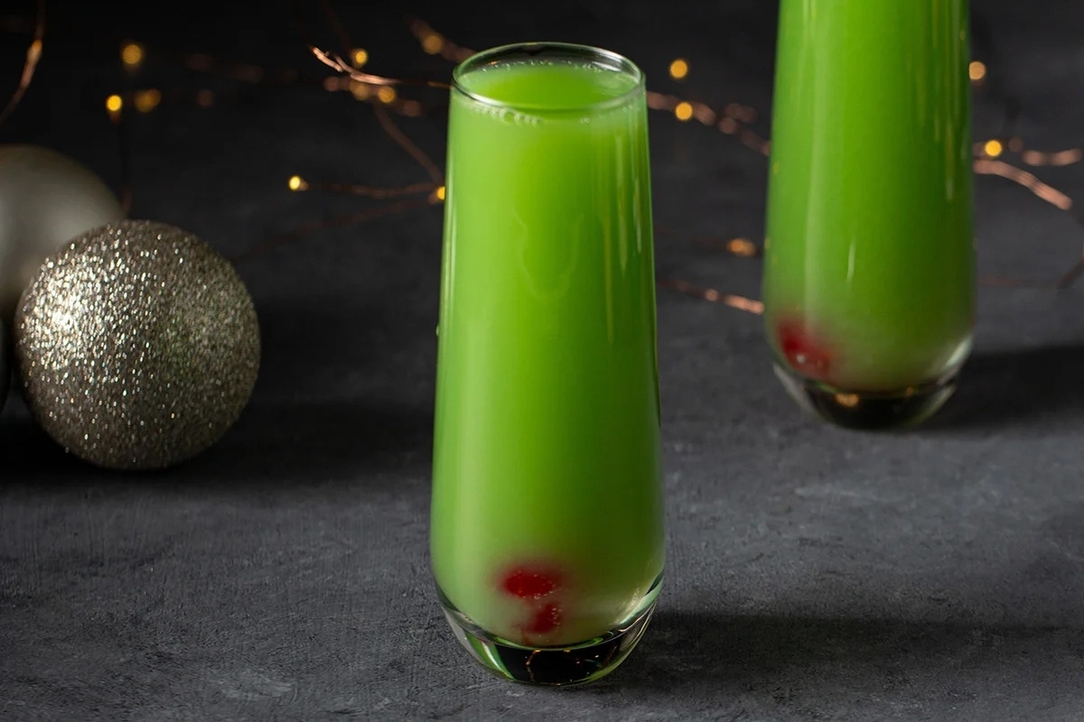 Two glasses of Grinch-inspired green liquid with Christmas decorations.