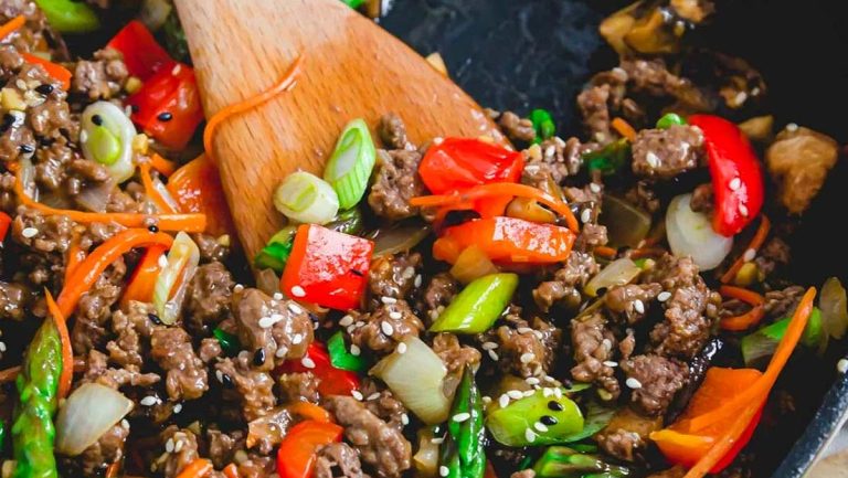 Beef stir fry in a skillet with vegetables and a wooden spoon.