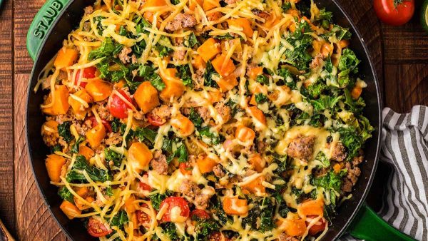 A skillet full of vegetables, meat and cheese.