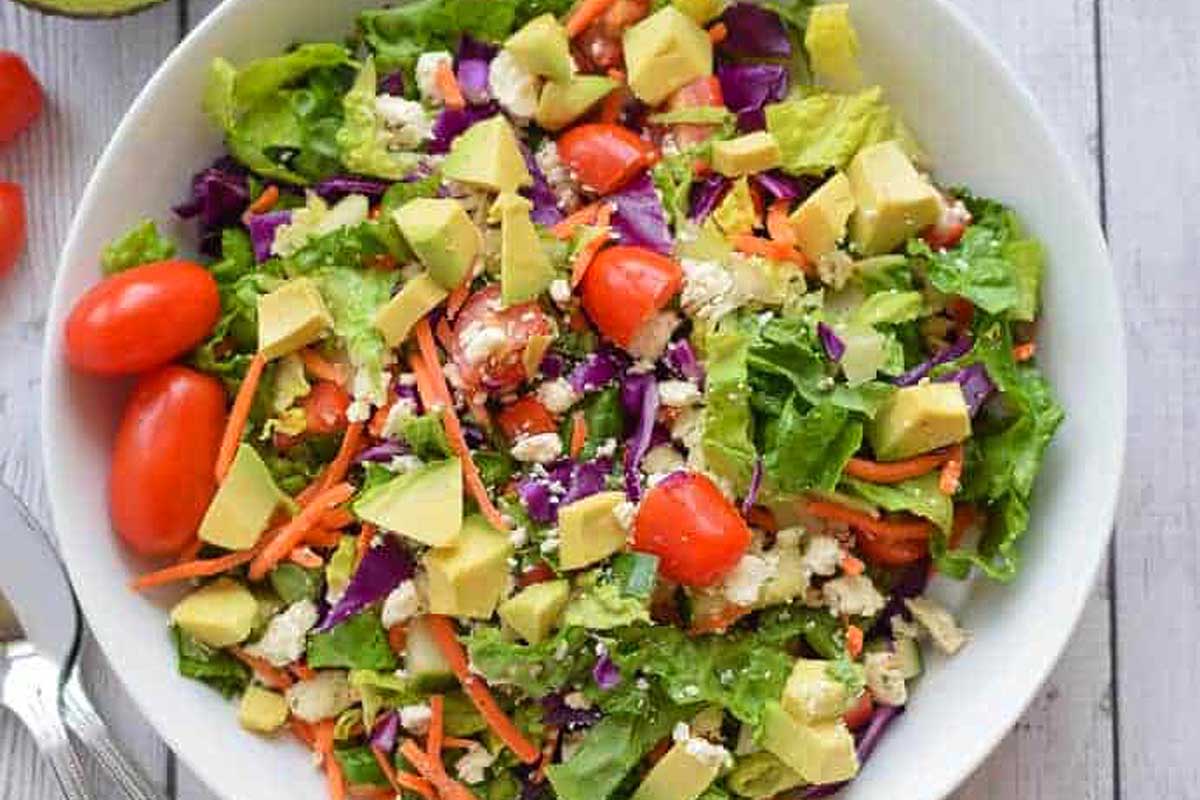 A bowl of salad with avocado, tomatoes and carrots.