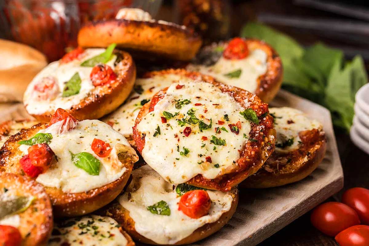 Pizza bagel bites on a tray with tomatoes and basil.