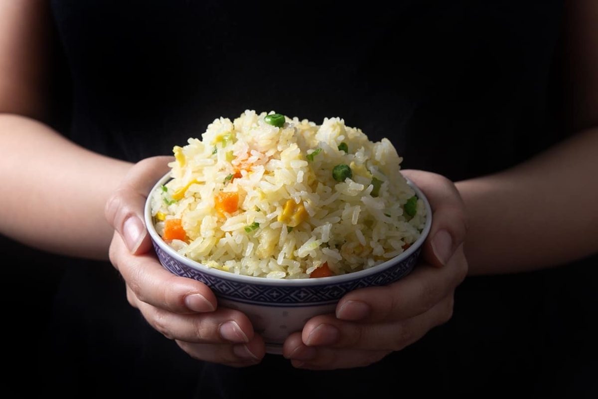 A woman is holding a bowl of fried rice made with frozen mixed vegetables.