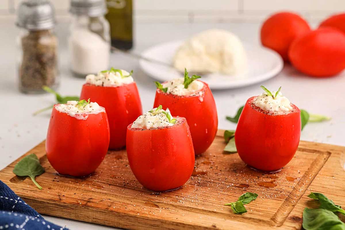Stuffed tomatoes with ricotta cheese and basil displayed on a cutting board, perfect for tomato lovers looking for new recipes.