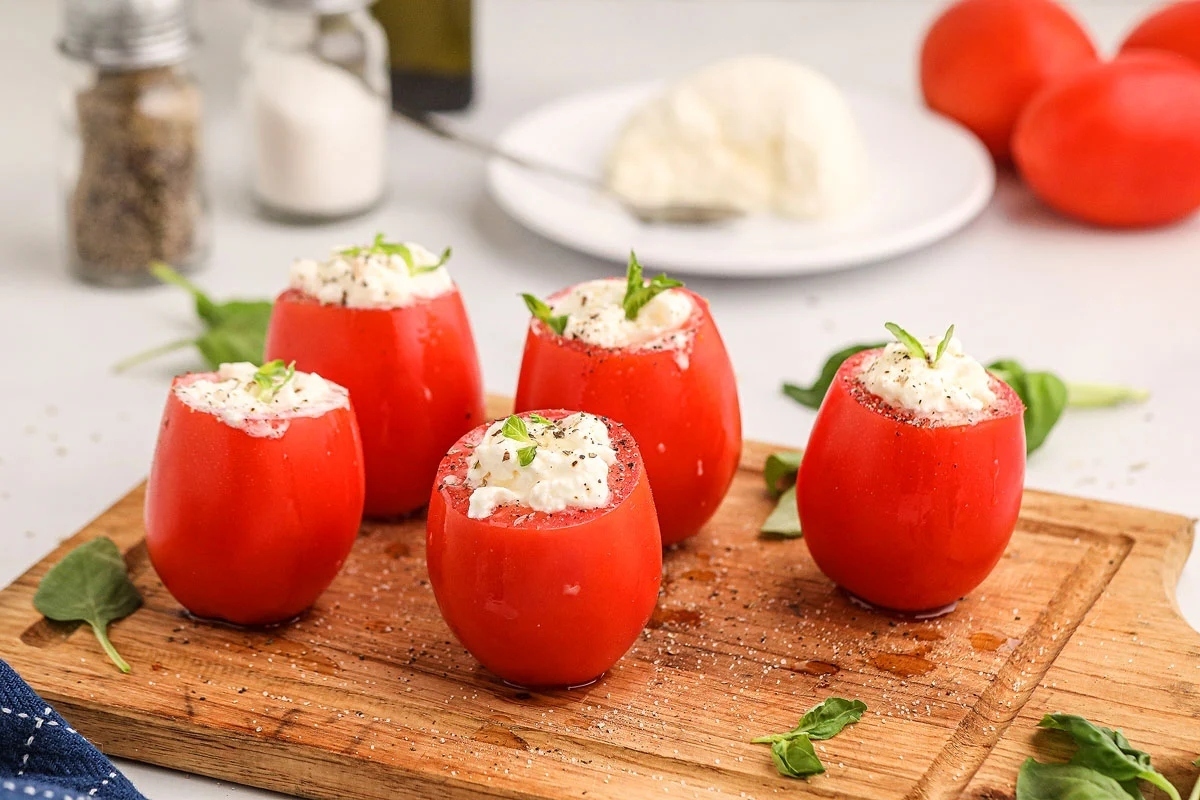 New Year's Eve appetizers - Stuffed tomatoes with ricotta cheese and basil on a wooden cutting board.