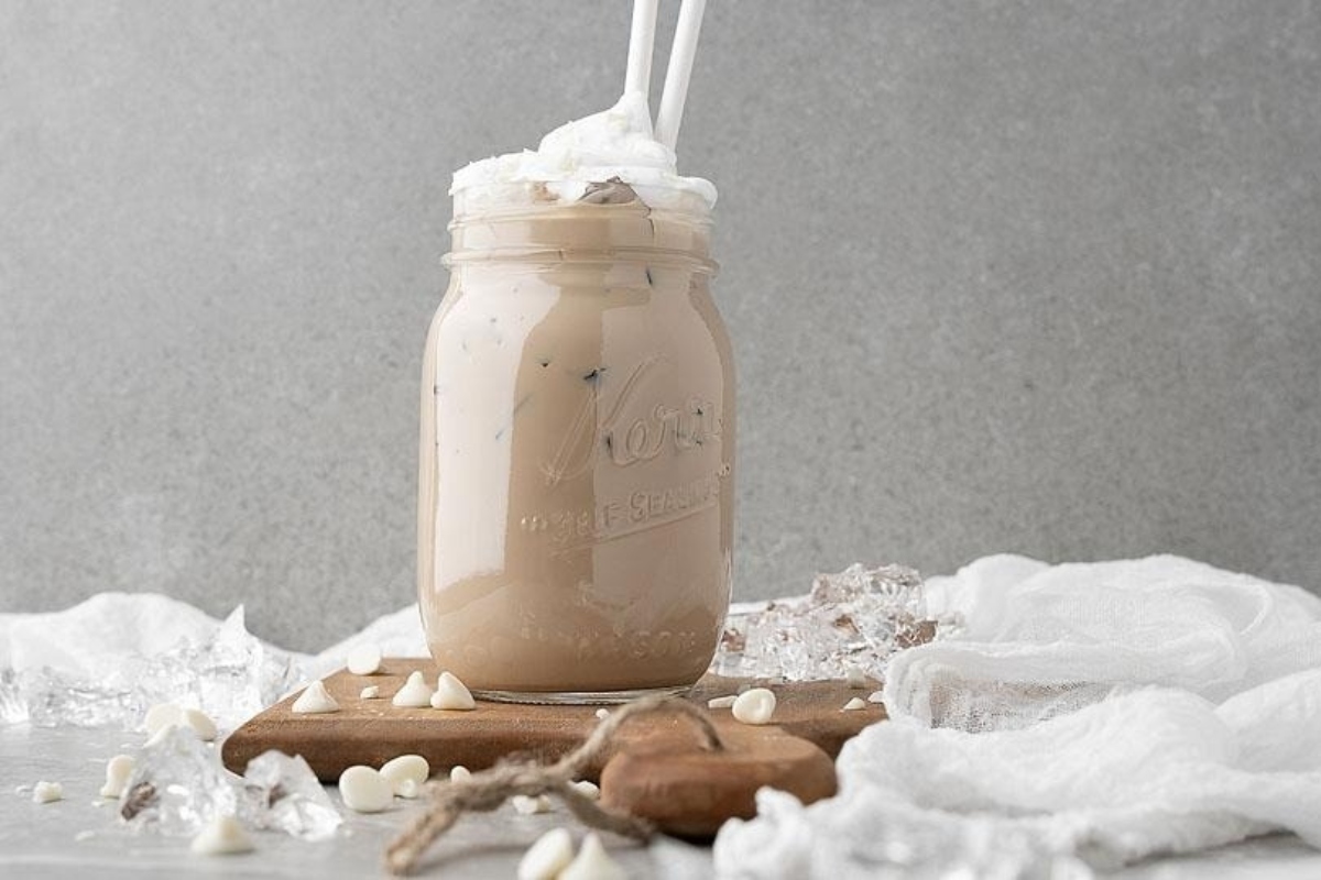 A delicious recipe for a white chocolate iced coffee in a mason jar topped with whipped cream.