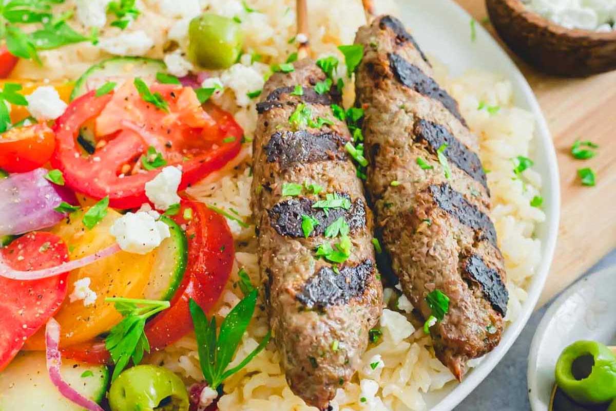 Greek meat skewers on a plate with rice and vegetables, also known as kebabs.